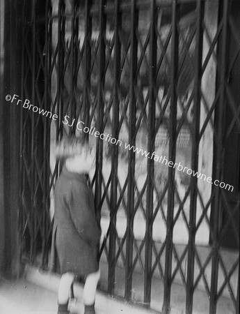 CHILD AT DOOR OF LIFT  OR SHUTTERED SHOP WINDOW